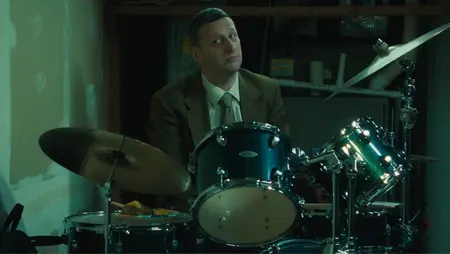 Comedian Tim Robinson makes a funny face while sitting at a large drum set in the black comedy FRIENDSHIP from A24, which is featured on the HBO Max September 2025 list of new movies and TV shows.