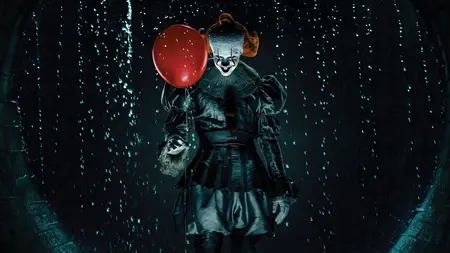 The evil clown Pennywise gives a sinister smile as he stands in the middle of a watery sewer while holding a red balloon on the official poster for the horror prequel series IT: WELCOME TO DERRY, which is included in the HBO Max October 2025 list of new movies and TV shows.
