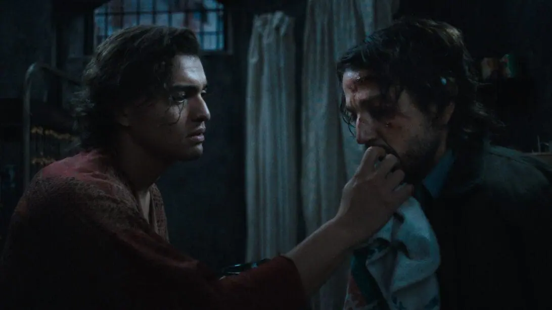 Tonatiuh holds up Diego Luna's injured face inside a grimy jail cell as the two portray political prisoners in 1983 Argentina in the movie musical adaptation of KISS OF THE SPIDER WOMAN. 