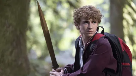 Walker Scobell stars as the young demigod Percy Jackson holding up a golden sword against a vibrant forest backdrop in PERCY JACKSON AND THE OLYMPIANS Season 2, which is included in the Disney+ and Hulu December 2025 list of new movies and TV shows.