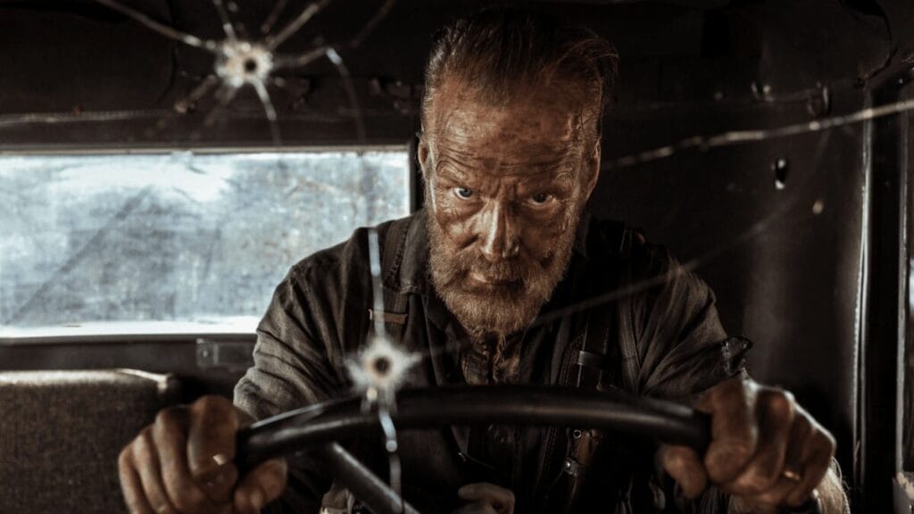 An intense close-up of Jorma Tommila as legendary Finnish army commando Aatami Korpi driving a battle damaged truck with a furious look of anger on his face in the movie sequel SISU: ROAD TO REVENGE.