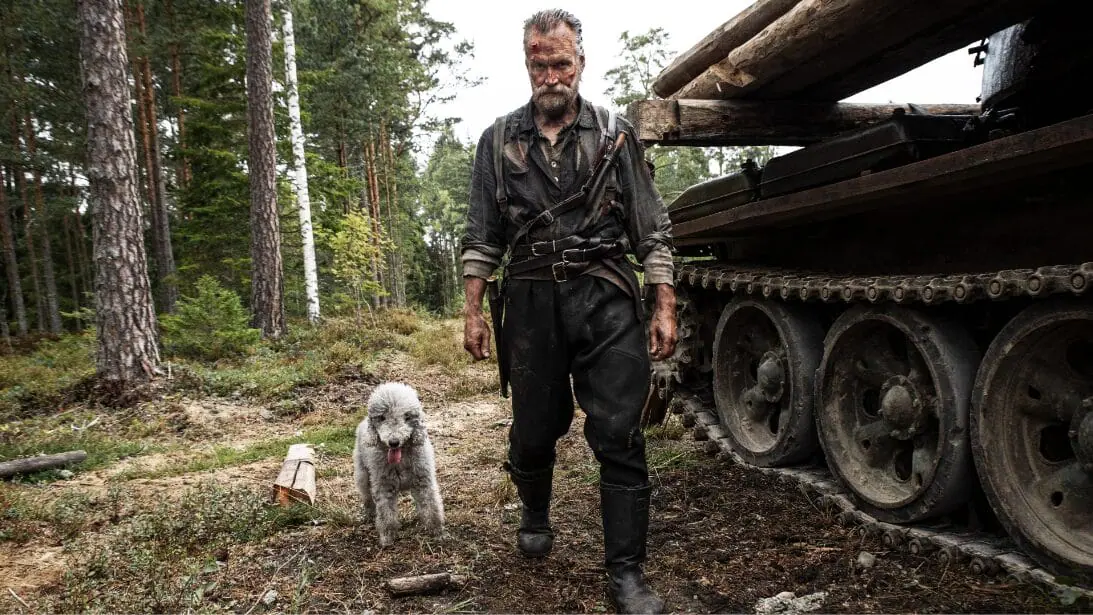 Jorma Tommila stars as legendary Finnish army commando Aatami Korpi posing next to a large tank in a battle field with his loyal and fluffy Bedlington Terrier in the action sequel SISU: ROAD TO REVENGE. 