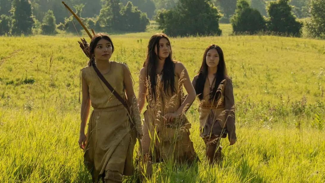 Three female members of the fictional Shokopiwah Native American tribe cross a large beautiful field in a historical flashback segment from episode 4 of IT: WELCOME TO DERRY.