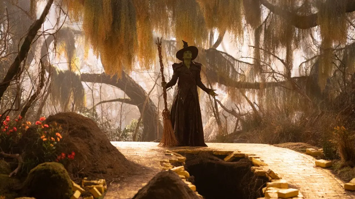 Cynthia Erivo as Elphaba Thropp, in her updated Wicked Witch of the West black costume, belts out a song in the middle of a beautiful forest with old brown trees in the movie musical sequel WICKED: FOR GOOD.