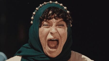 A shot of Alia Shawkat screaming into the camera while dressed as an Iraqi towns-person with a traditional head scarf in the hilarious war satire film ATROPIA.