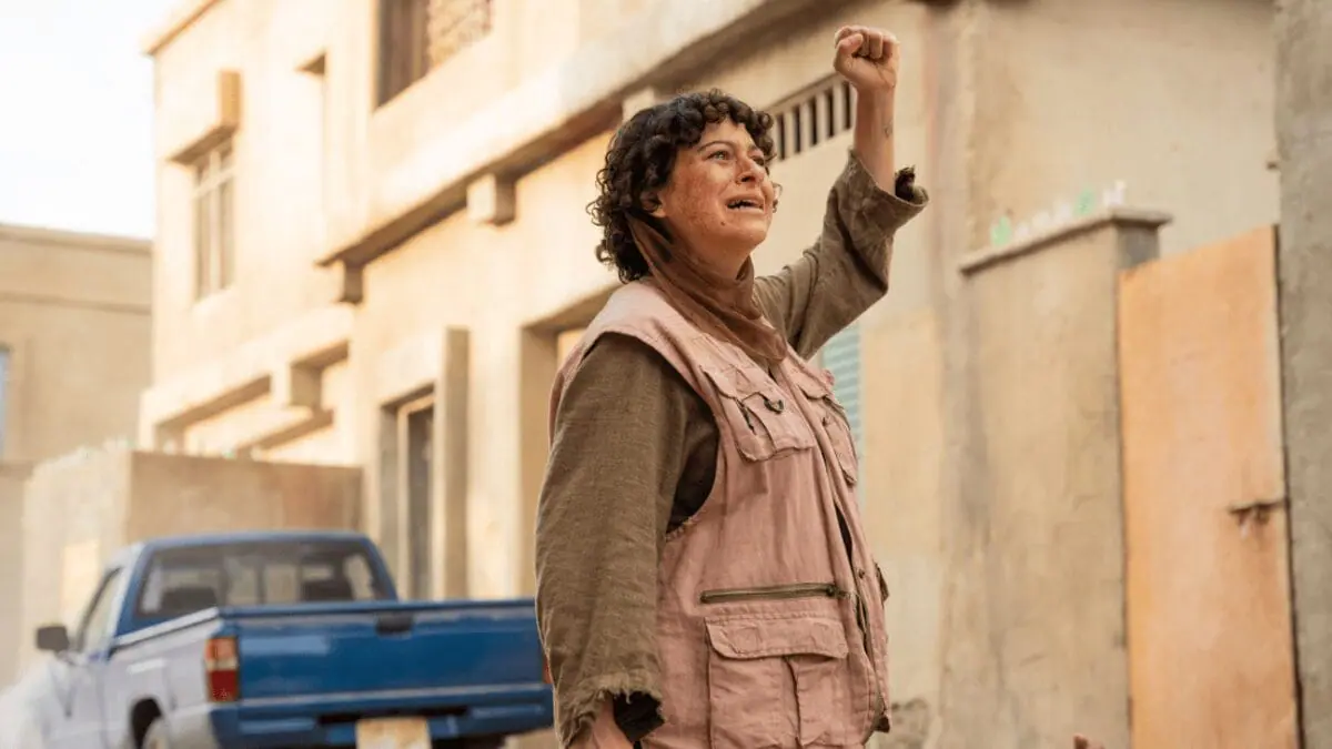 Alia Shawkat raises her fist in the air with a scared look on her face as she pretends to act in the middle of a Middle Eastern war simulation in the movie ATROPIA.