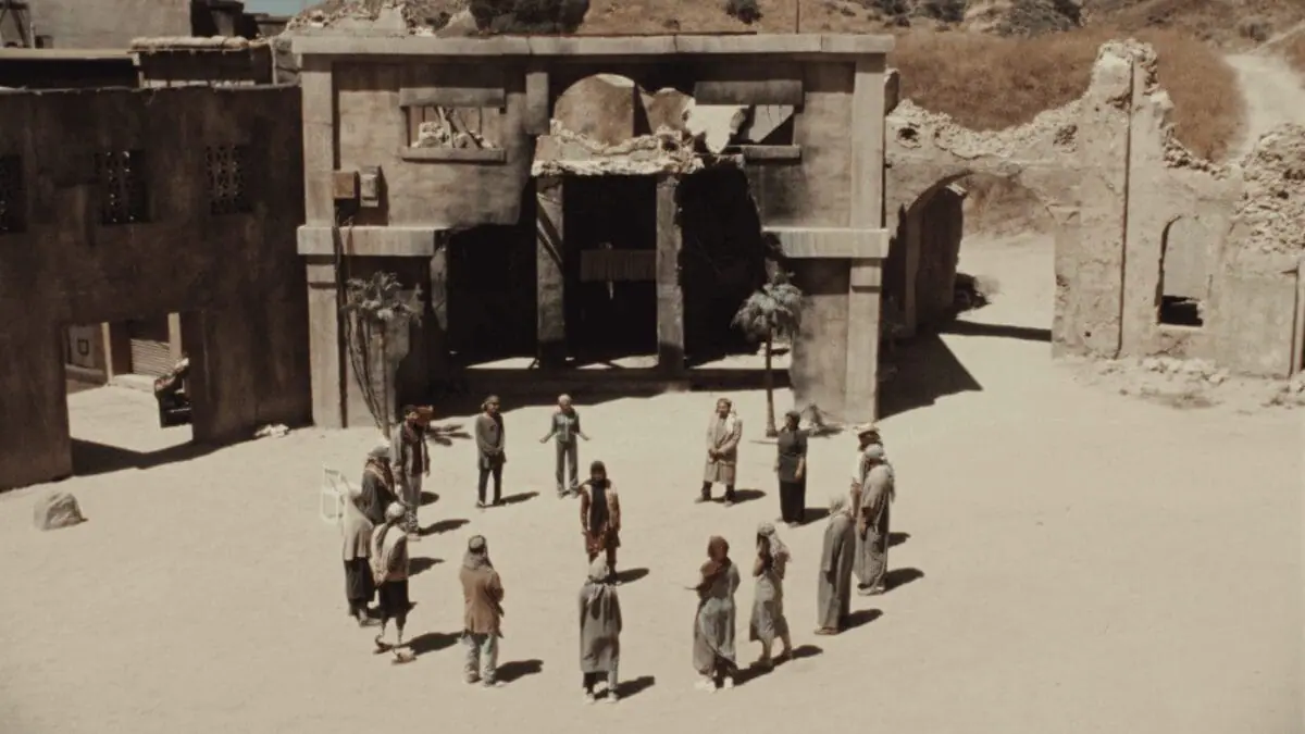 A group of actors dressed as Middle Eastern civilians come together and form a circle in the center of a fake desert town meant to simulate the country of Iraq in the war satire movie ATROPIA.