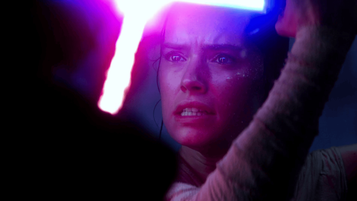 A dramatic close-up shot of Rey's face lit by the blue Skywalker lightsaber as she struggles to hold back Kylo Ren's red lightsaber during their climactic duel in STAR WARS: THE FORCE AWAKENS. 