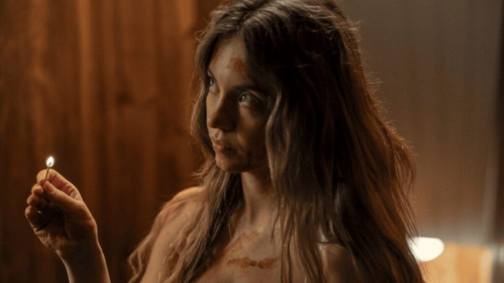Sydney Sweeney holds up a small lit match, revealing her messy hair and that she might be covered in blood, in the psychological thriller THE HOUSEMAID. 