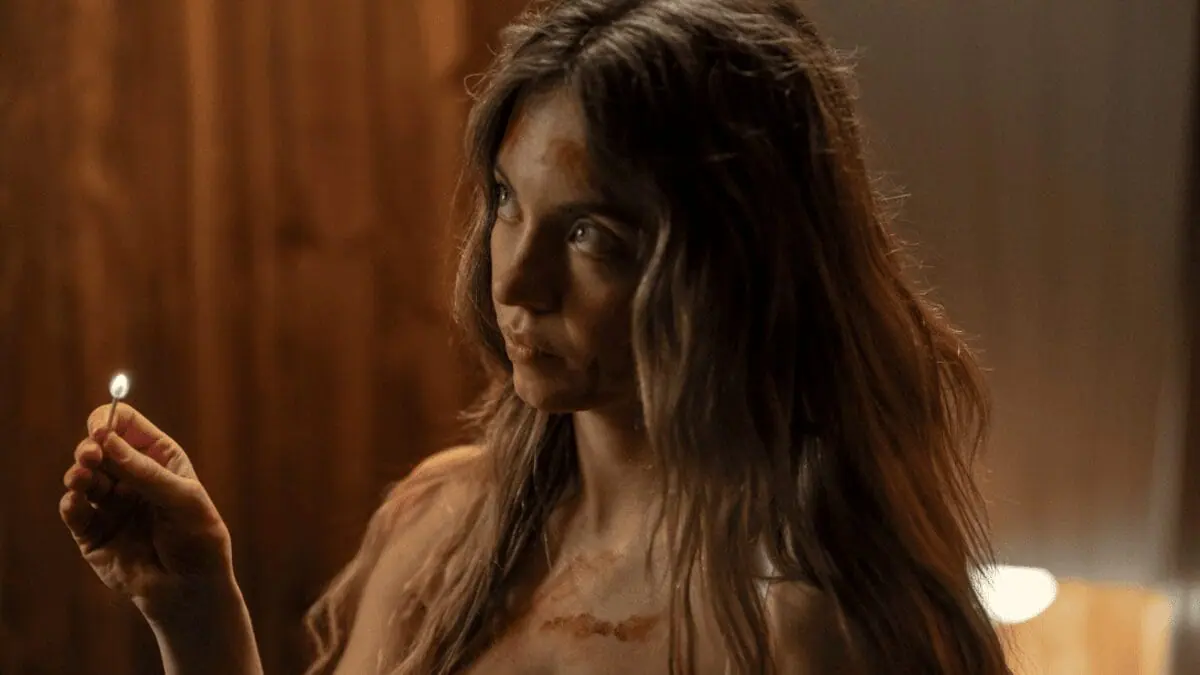 Sydney Sweeney holds up a small lit match, revealing her messy hair and that she might be covered in blood, in the psychological thriller THE HOUSEMAID. 