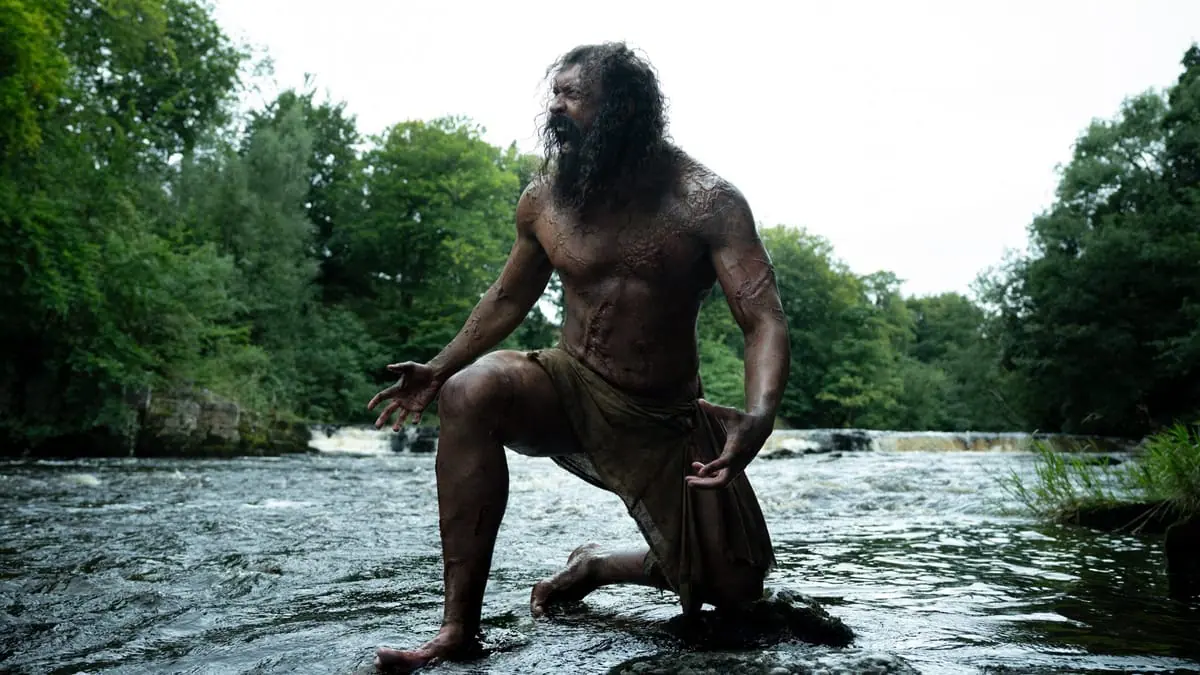 The Infected Alpha zombie named Samson lets out a powerful roar as he kneels by a large river in the forest in the movie 28 YEARS LATER: THE BONE TEMPLE.