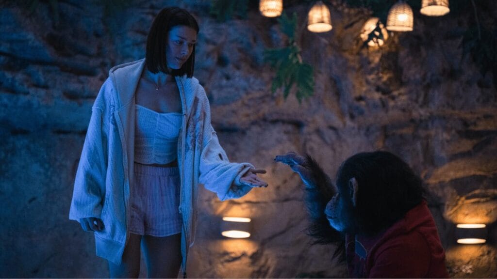 Jessica Alexander and Ben the chimpanzee reluctantly hold out to hold each other's hand by a swimming pool in the horror film PRIMATE. 