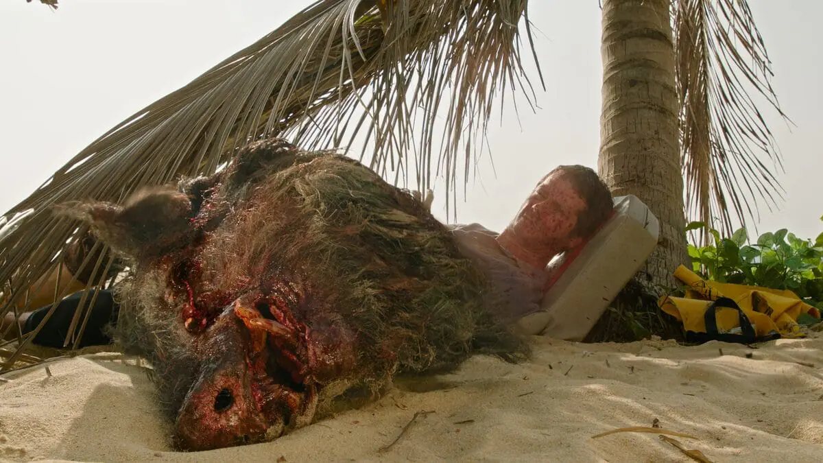 The bloody decapitated head of a large boar sits in front of Dylan O'Brien's shocked face in the horror thriller film SEND HELP.