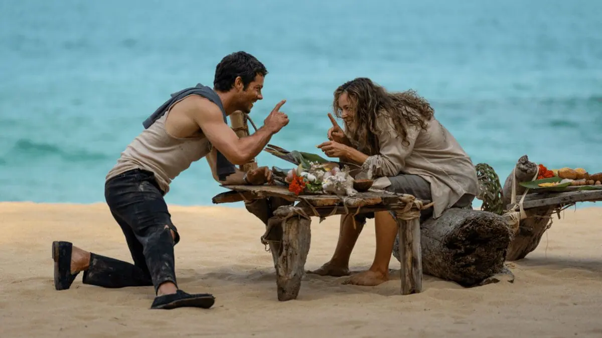 Dylan O'Brien and Rachel McAdams argue with each other while having a fish feast on a deserted island beach in the survival thriller movie SEND HELP. 