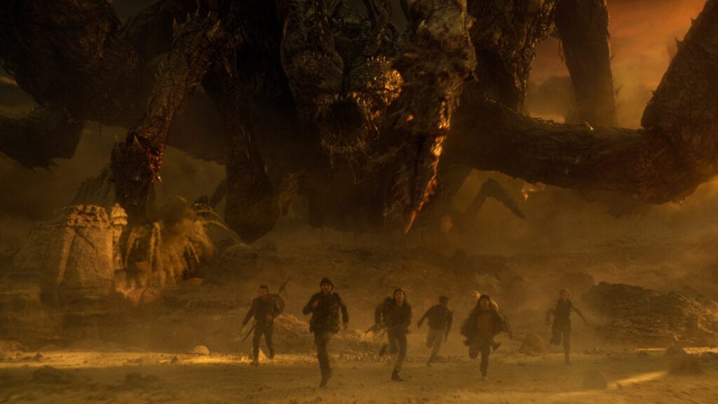 A wide CGI-heavy shot of the Hawkins gang running away from the giant Mindflayer monster in Dimension X from the final episode of STRANGER THINGS.