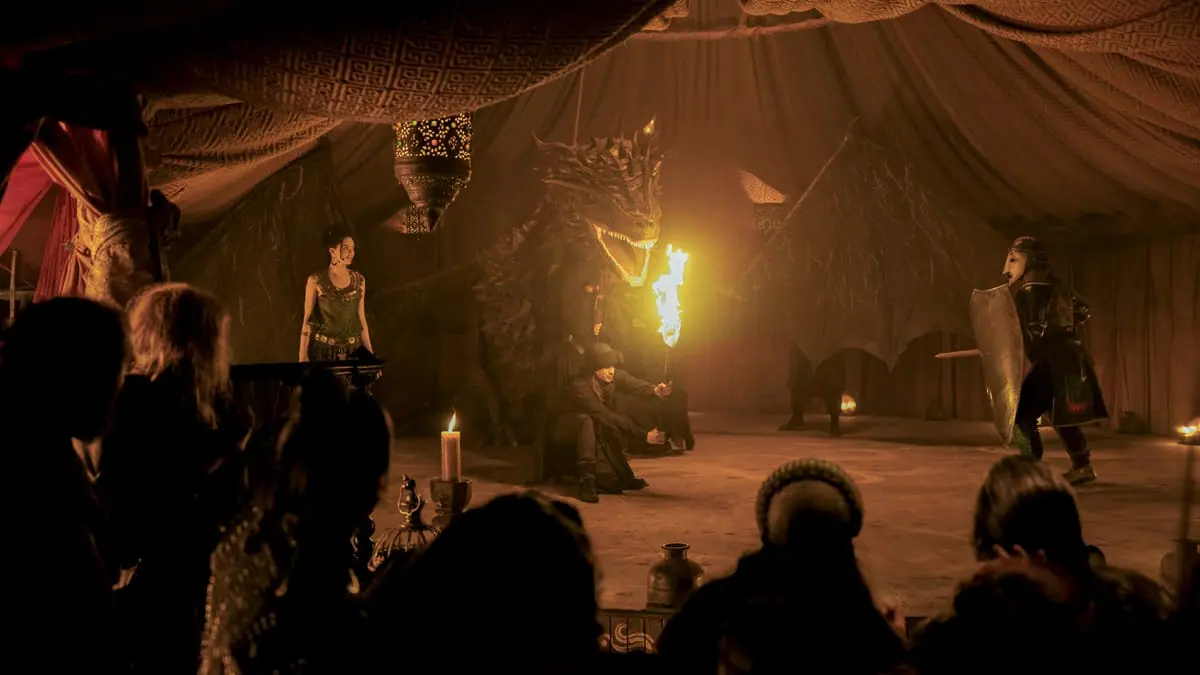 An excited crowd watches a renaissance show with a large dragon puppet an actor dressed as a silver knight in the HBO fantasy series A KNIGHT OF THE SEVEN KINGDOMS.   