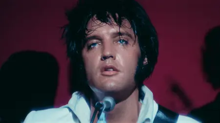 A close-up shot of Elvis Presley looking tired and sweaty during a live performance on stage while wearing his iconic white leather jacket in the music documentary EPiC: ELVIS PRESLEY IN CONCERT.