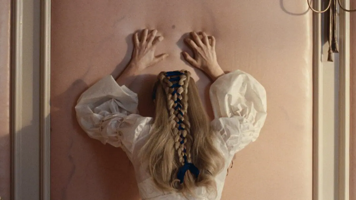 Margot Robbie throws her arms and hands up against a pink wall in total distress in Emerald Fennell's WUTHERING HEIGHTS film adaptation.