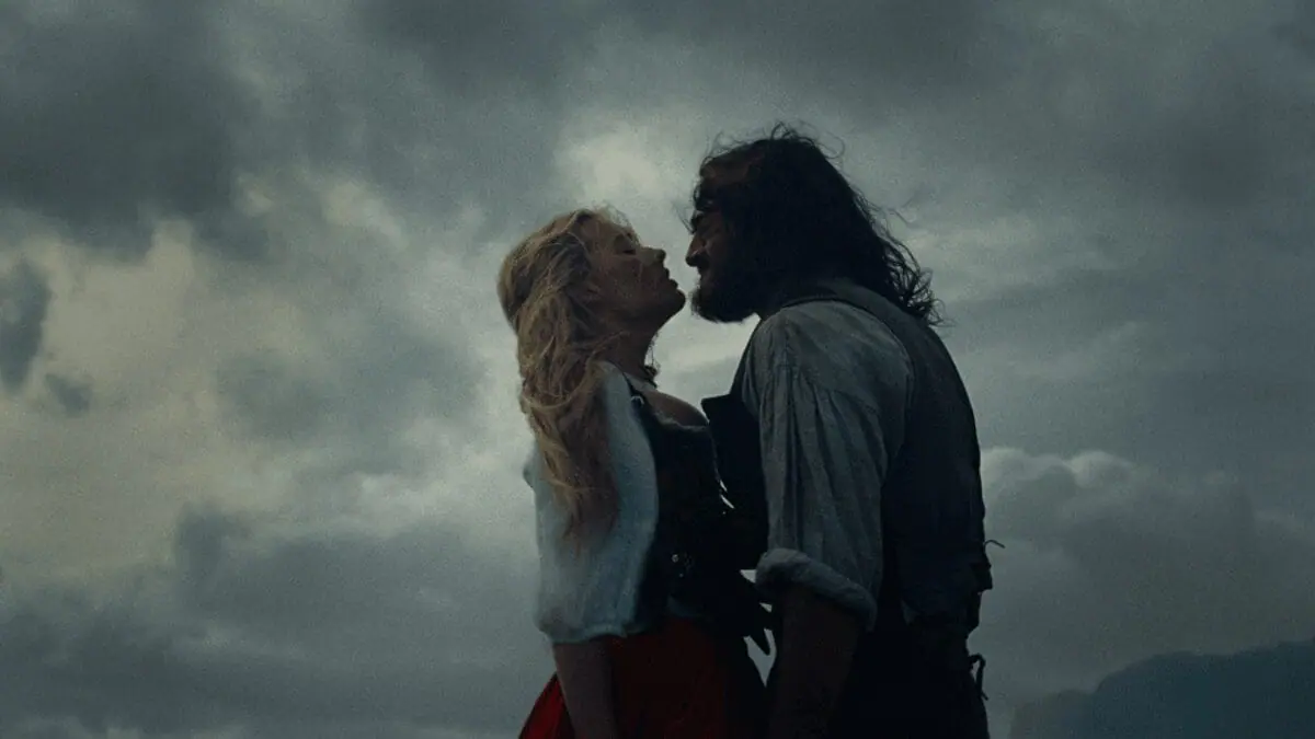 Margot Robbie and Jacob Elordi embrace each other romantically against a moody backdrop of dark stormy clouds in Emerald Fennell's WUTHERING HEIGHTS movie adaptation. 