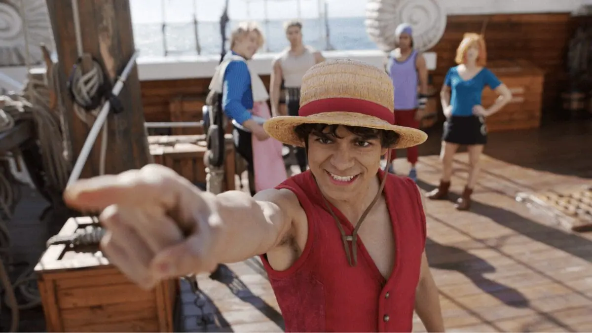 Iñaki Godoy points towards the screen as he leads the Straw Hat Crew as Monkey D. Luffy while Nami, Roronoa Zoro, Usopp, and Sanji stand behind him on their pirate ship in ONE PIECE Season 2.