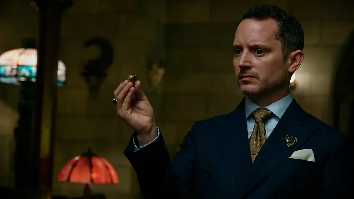 Elijah Wood stars as The Lawyer holding up a mysterious gold ring while making a stern face in the horror sequel READY OR NOT 2: HERE I COME.