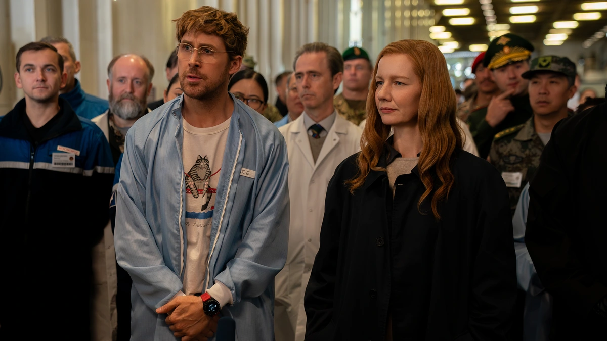 Ryan Gosling and Sandra Hüller stand next to each other looking concerned during a meeting with top NASA scientists in PROJECT HAIL MARY.