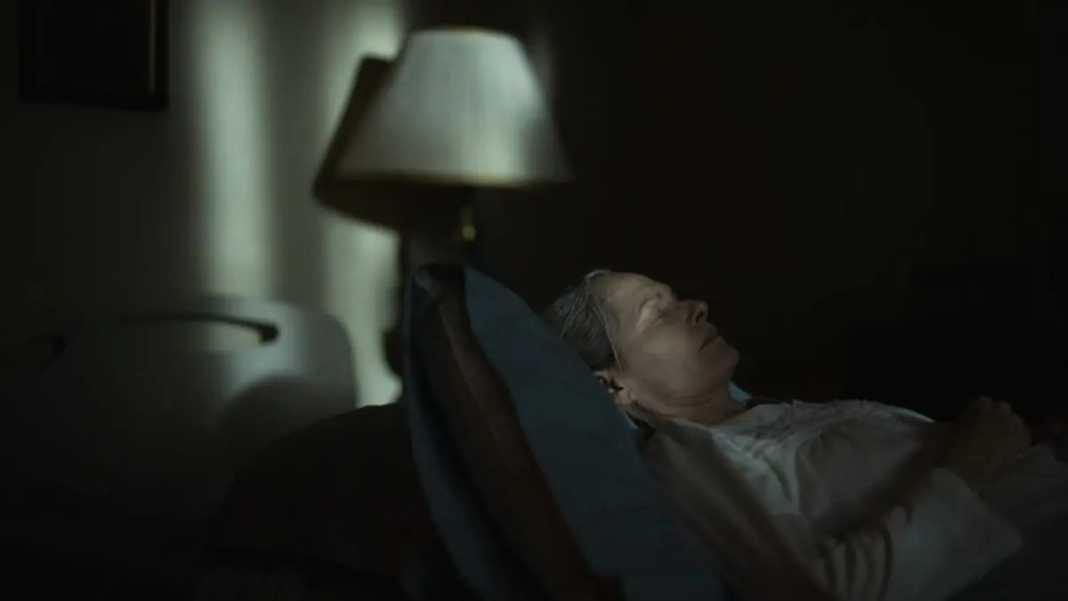 A creepy shot of Michèle Duquet sleeping comatose in a dark bedroom from the A24 horror movie UNDERTONE. 