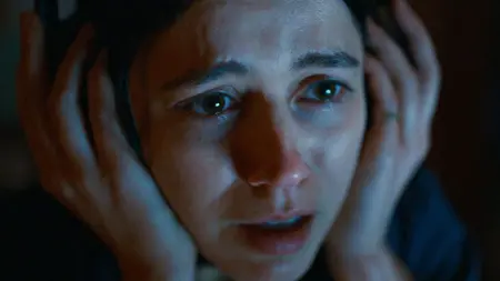 A close-up shot of Nina Kiri's face looking incredibly scared as she holds her headphones tight with fear from the A24 horror movie UNDERTONE.