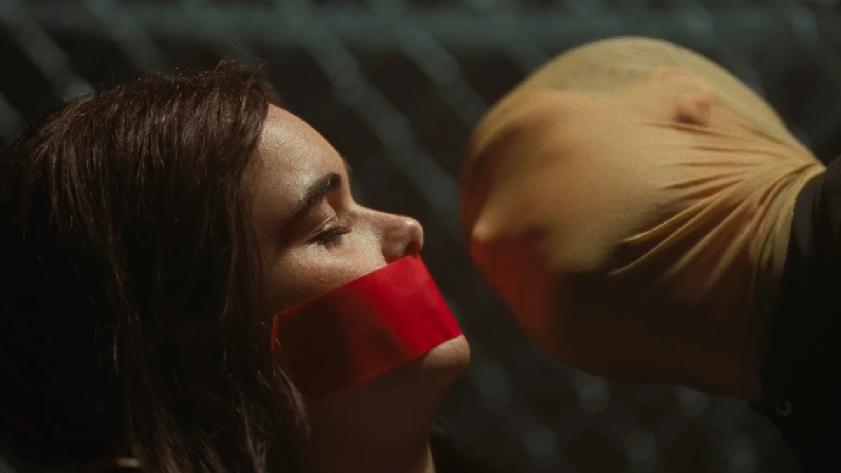Barbie Ferreira sits hostage with her mouth covered in red cloth while a demented Dacre Montgomery wearing a ski mask puts his face up to hers in FACES OF DEATH (2026). 