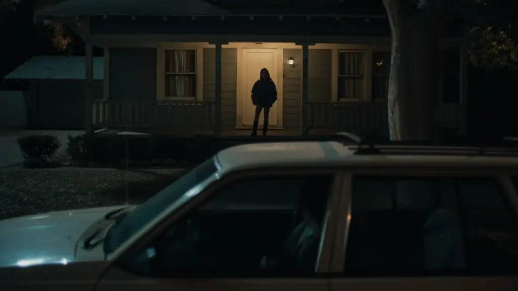 A shot of the crazy obsessed girlfriend Nikki watching her poor boyfriend Bear from her porch while he sits in his car in fear from the horror movie OBSESSION.
