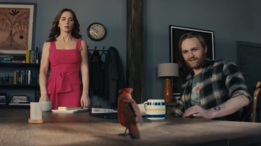 A mysterious, small red cardinal bird sits on a table between Emily Blunt and Wyatt Russell in the sci-fi thriller DISCLOSURE DAY.