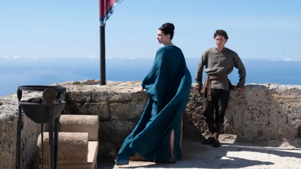 Anne Hathaway stars as Penelope and Tom Holland stars as Telemachus standing together in the beautiful Greek palace of Ithaca in Christopher Nolan's THE ODYSSEY. 