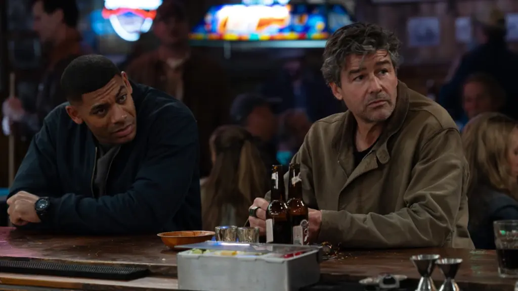 Aaron Pierre and Kyle Chandler as John Stewart and Hal Jordan sit at a bar together in the DC comic-book series LANTERNS on HBO.
