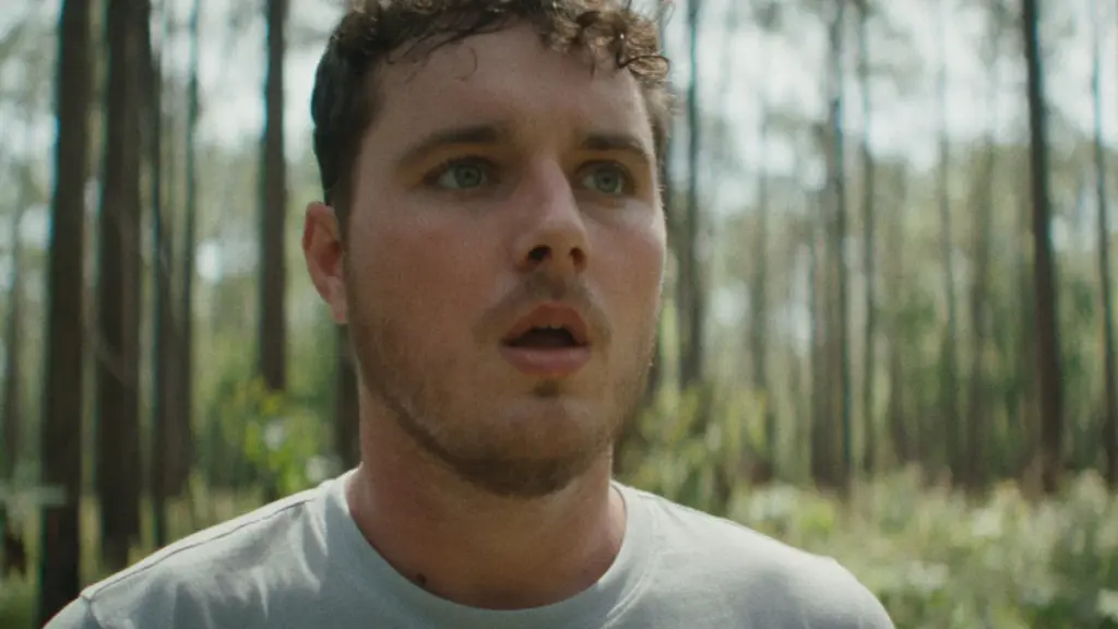 Mitchell Cole stars as the character Tyler making a shocked facial expression in the middle of a dense forest filled with trees in the horror movie IT ENDS.