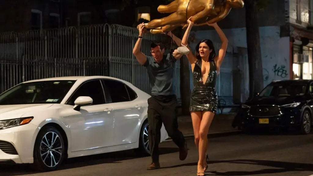 Callum Turner and Monica Barbaro get into hijinks as they run across the New York City streets holding up a large golden figure in ONE NIGHT ONLY. 