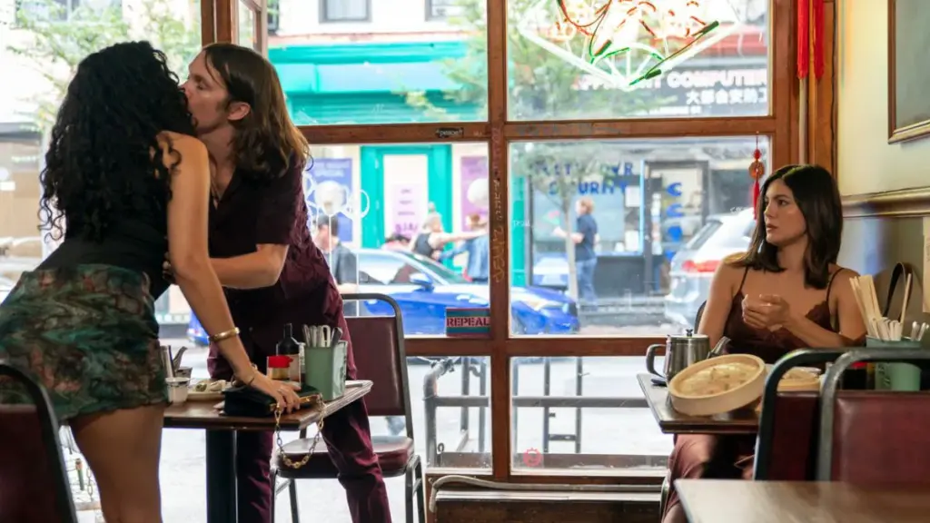 Monica Barbaro makes a hilariously surprised face as two strangers make out passionately next to her inside a NYC cafe in the romantic comedy ONE NIGHT ONLY.